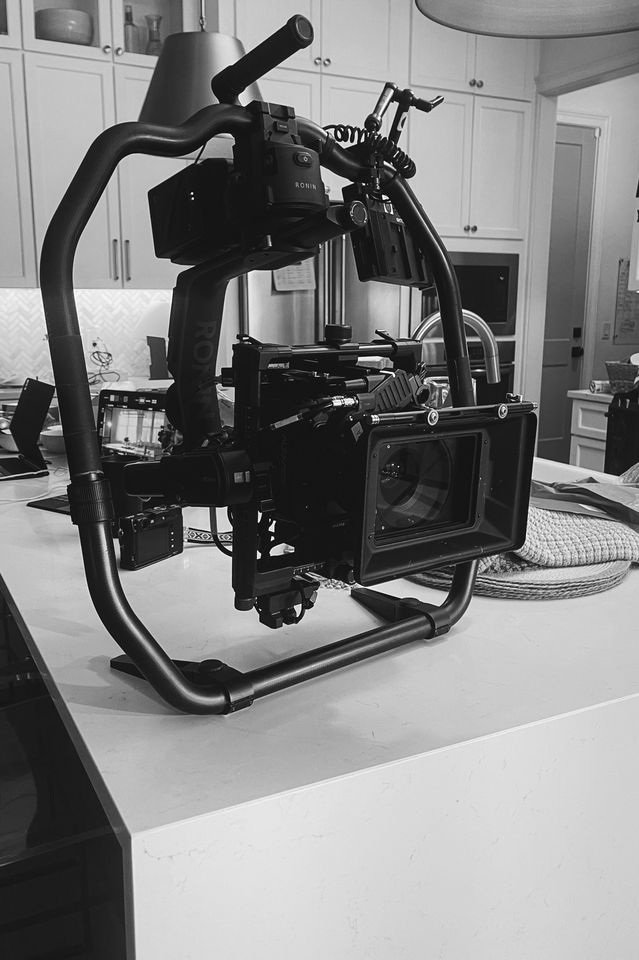 Black and white photo of a professional camera mounted on a stabilizer rig set up on a kitchen countertop.