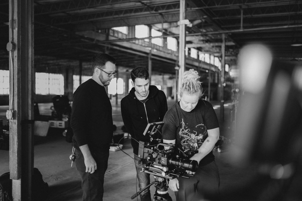 Three people working with a professional camera in an industrial warehouse setting.