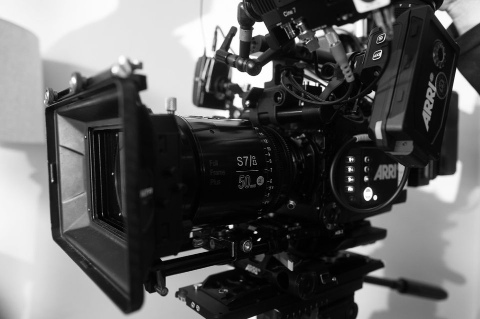 Black and white professional cinema camera with various attached components, including a lens and monitor, mounted on a rig.