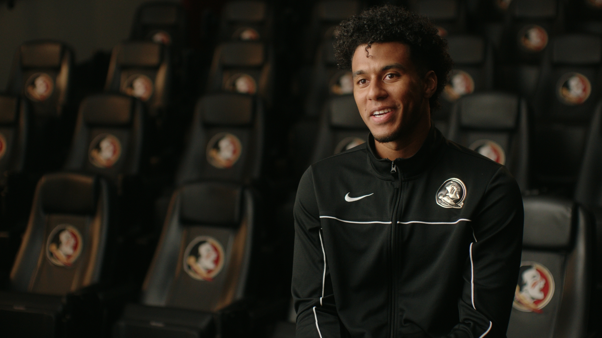 Jordan Travis in Florida State locker room, smiling in a Nike track jacket