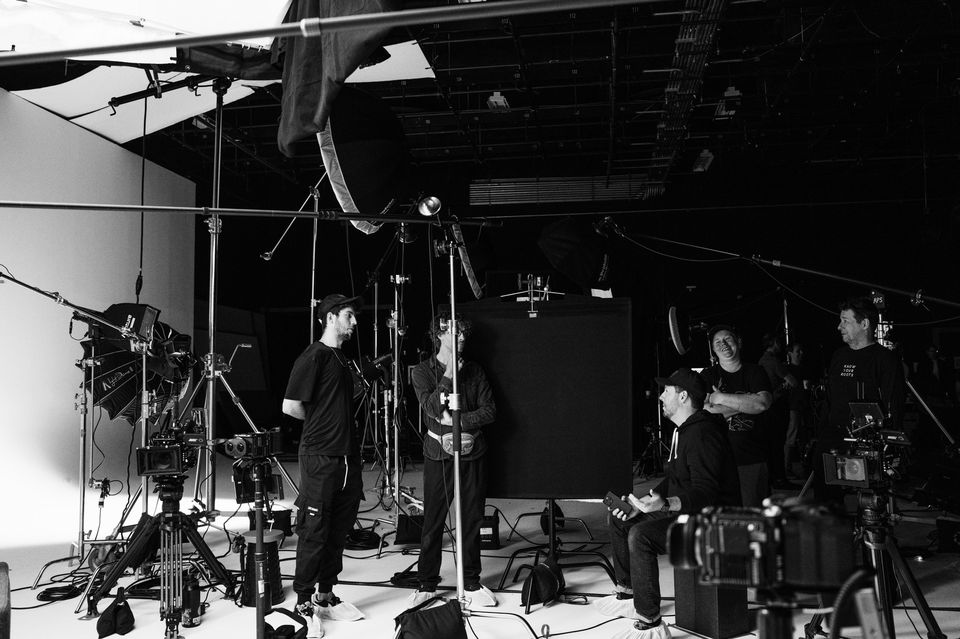 Behind-the-scenes of a film or photo shoot with crew members and equipment in a black and white studio setting.